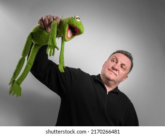 A Plush Soft Green Toy Frog In The Hands Of A Man.