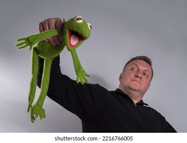 A Plush Soft Green Toy Frog In The Hands Of A Man.