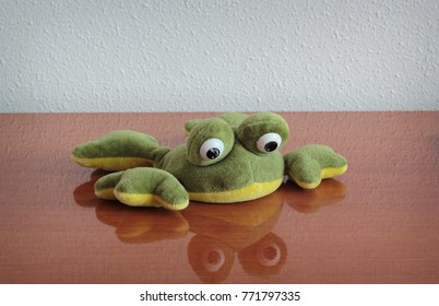 Plush Toy Frog Lying At The Table. Shallow Depth Of Field.