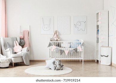 Plush Toy And Pillow On White Round Carpet In Baby's Room With Grey Armchair And Posters On Wall