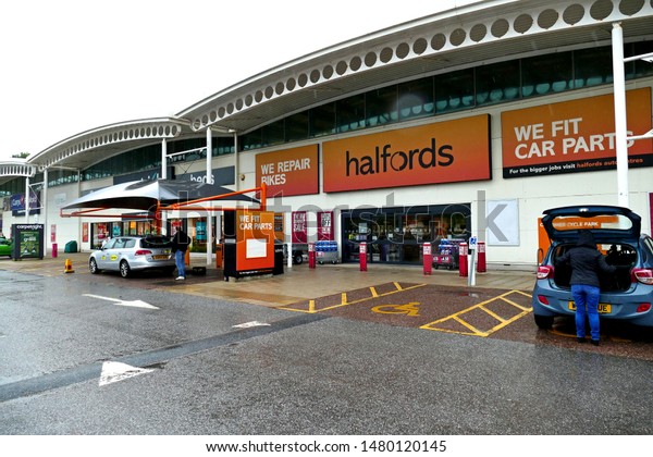 Plymouth England August\
2019. Halfords full facade. Retailer of car parts and accessories.\
Canopy with car under having parts fitted. Parking bays.  Large\
orange signage.