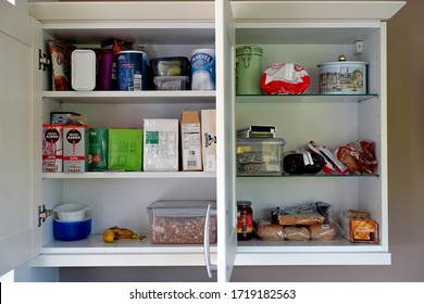 Plymouth England. Interior of a kitchen double wall cupboard. Three shelves, plastic boxes of cereal, dried milk, bread rolls, biscuits, tins, packets of coffee. Porridge, crisps, banana.