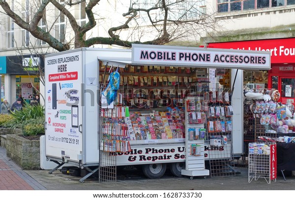 Plymouth\
England.  Portable cabin in pedestrian area that sells mobile phone\
accessories and repairs cracked mobile phone screens. Large drop\
down front panel with shelves of\
products.