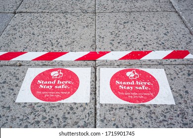 Plymouth, UK. 27/4/20: Signs On A Concrete Pavement Read Stand Here Stay Safe With A Line Of Red And White Tape To Remind People Of The Two Metre Rule.