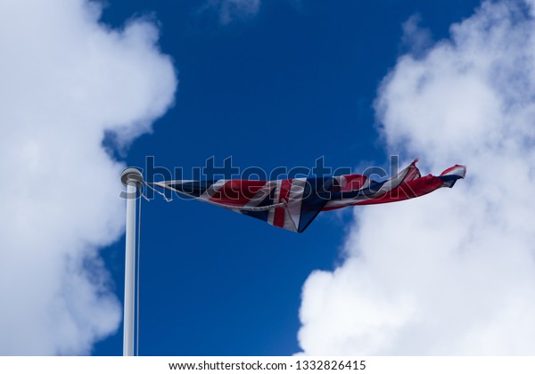 Plymouth UK. 3/7/19: A Union Jack Flag hanging\
on by a thread flies on a windy\
day.