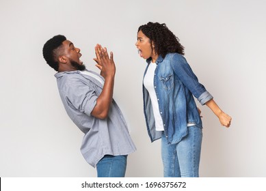 PMS Concept. Mad African American Woman Yelling At Her Scared Boyfriend, Shouting With Rage On Light Studio Background, Empty Space