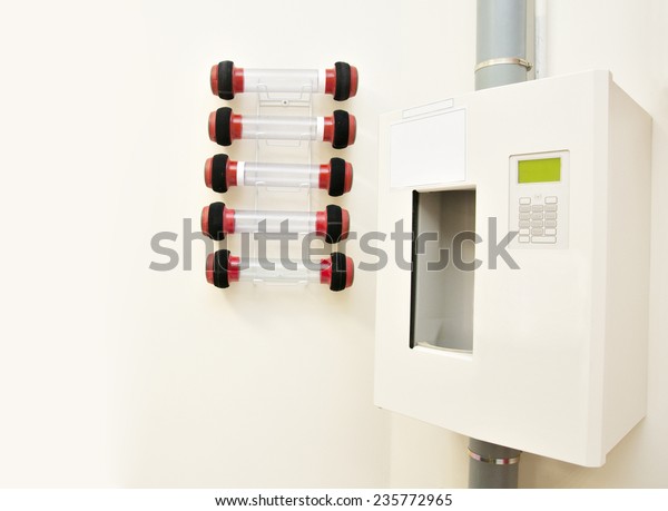 A Pneumatic Tube Transfer\
System Station and a row of empty capsules attached to a building\
wall.