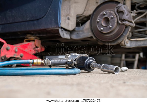 Pneumatic wrench\
tool on the asphalt and a car jack for lift up the body and\
changing the tire. Car without\
wheel