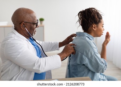 Pneumology Consultation Concept. Black male general practitioner examining coughing female patient in modern clinic, using stethoscope, listening lungs from the back. Medicine And Healthcare - Powered by Shutterstock