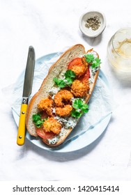 Po' boy sandwich with crispy cornmeal shrimp, tomatoes, cilantro and mayo herbs sauce on light background, top view