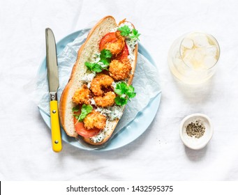 Po' boy sandwich with crispy cornmeal shrimp, tomatoes, cilantro and mayo herbs sauce on light background, top  view     