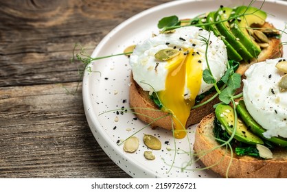 Poached egg on bread with spinach, avocado and pumpkin seeds on the wooden table, Healthy food, keto diet, diet lunch concept. Top view.