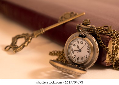 A pocket watch and a key resting against an old book. a concept of time and freedom.