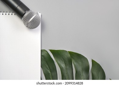 Podcast Concept. Black Microphone, Content Notebook, Monstera Leaf. Audio Music Device. Recording Production Flatlay. School Knowledge Equipment. Home Online Teaching. Grey Background