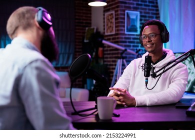 Podcast presenter having live conversation with young man, recording discussion for audience on internet channel. Male influencer enjoying chat with guest, broadcasting with production equipment. - Powered by Shutterstock