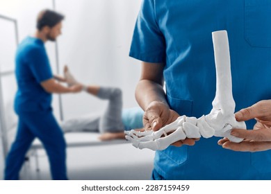 Podiatrist showing anatomical foot skeleton model during his assistant examination injured leg of patient in department of traumatology and orthopedics