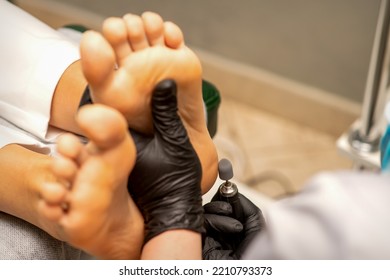 Podiatrist wearing black protective gloves cleaning the skin of foot from callus and corn with the professional electric tool - Shutterstock ID 2210793373