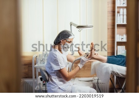 Podologist foot doctor in mask on face, making procedure for foot with special equipment