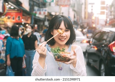 Poeple travel and eating street food concept. Happy young adult asian foodie woman holding spicy grilled squid at southeast asia Chinatown market. - Shutterstock ID 2151398971