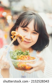 Poeple Travel And Eating Street Food Concept. Happy Young Adult Asian Foodie Woman Holding Spicy Grilled Squid At Southeast Asia Chinatown Market.