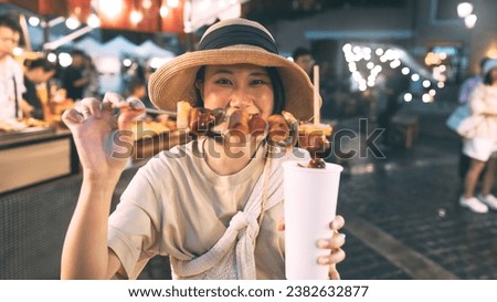 Poeple travel and eating street food concept. Happy young adult asian foodie woman holding bbq grilled skewers at outdoor vendor night market.