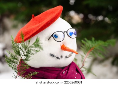 Poetry snowman. Close up photo with a snow man build in the court yard against green trees, dressed in literature style with glasses, scarf and bonnet.
