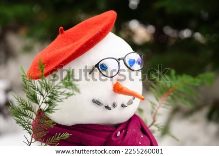 Poetry snowman. Close up photo with a snow man build in the court yard against green trees, dressed in literature style with glasses, scarf and bonnet.