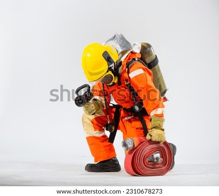 Pofessional firefighter is sitting turned sideways kneeling down holding a fire hose and wearing an oxygen tank on his back while looking at the floor on a white background.