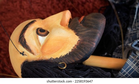 pofile wooden head of a puppet or marionette, bald, with beard and open eyes hanging in the strings isolated over a red carpet background - handmade painted vintage toy - Shutterstock ID 2258193647