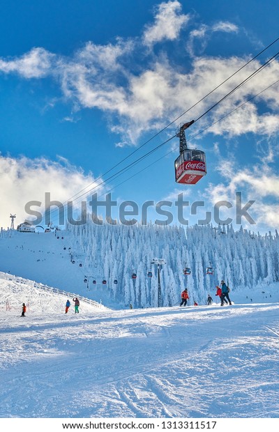 Poiana\
Brasov, Romania -‎22 ‎gennaio 2019:Red cable car in a ski resort,\
Skiers and snowboarders enjoy the ski slopes in winter resort whit\
forest covered in snow,Poiana\
Brasov,Romania