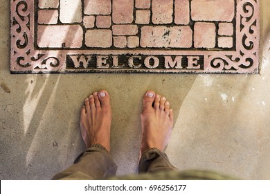 
Point Of View Of Bare Feet At Home Front Door Welcome Mat On Concrete Patio.