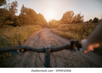 Point of view bike riding at the rural area during summer sunset. Concept of summertime sport adventures using mountain bike. Blurred silhouette of bicycle handlebar.