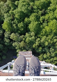 Point of view looking down from a high metal platform onto a lush green forest canopy