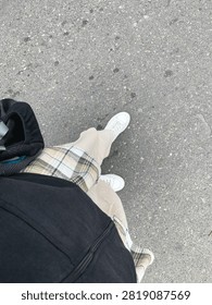 Point of view looking down at a person's feet wearing white shoes standing on an asphalt road.