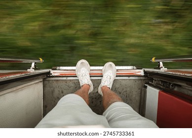 Point of view from open train door with male legs in white sneakers and motion blurred green landscape. Adventure travel concept in Sri Lanka, dynamic journey and freedom feeling.