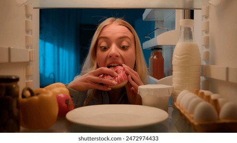 Point of view POV from inside refrigerator hungry Caucasian woman girl at night evening kitchen open fridge take out eating sweet donut unhealthy nutrition obesity diet failure overeating food addict