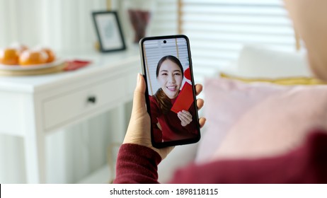 Point Of View Selfie Videocall Shot Of Attractive Beautiful Young Asian Lady In Red Chinese New Year Celebration Outfit Happy Smile Talk And Looking To Camera Mobile Phone Wishing For Lunar Festival.