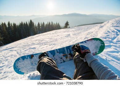 Point of view shot of a female snowboarder lying on the snow on the slope relaxing after riding, enjoying stunning view of winter mountains and sunset POV concept