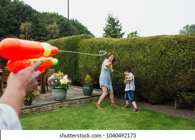 Point of view shot of a man having a water fight with water pistols in the garden with his wife and son.