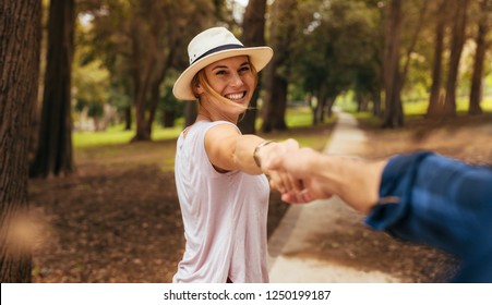 Point of view shot of romantic couple walking in park together. Man holding hands his happy girlfriend wearing a hat and smiling. Point of view shot.