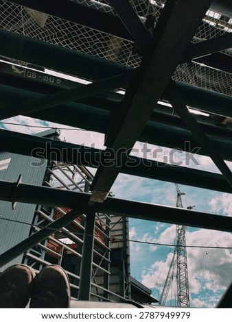Point of view shot of a worker sitting under heavy steel beam structure looking at the sky on a construction site.
