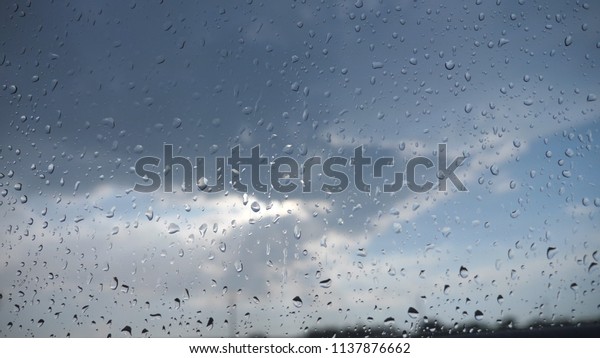 Point of view through the windshield of car with\
raindrops to the cloudy sky. Close up of water droplets on\
windowpane of vehicle in rainy\
day.
