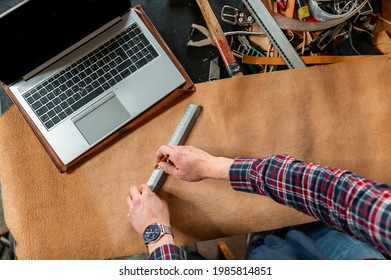 Point Of View Unrecognizable Man Working With Leather Measuring The Mockup. Workplace With Tools And A Computer Laptop.