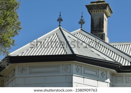 POINTED FORGED METAL SPIRE FINIAL ON A METAL PITCHED ROOF - Rooftop finished with ornate cast wrought iron curled decorative designed roof fixtures on a classical heritage historic house