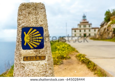 A pointer for the orientation of the Camino de Santiago pilgrims in Cape Finisterre. Finish zero Kilometers. In the background a lighthouse (faro) and an ocean. buen camino peregrino