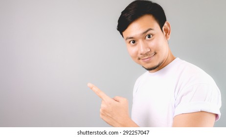 A pointing at content, empty copyspace. An asian man with white t-shirt and grey background.