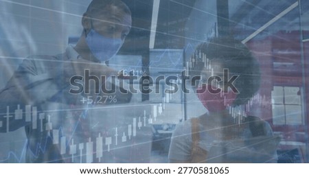 Pointing duo analyzing candlestick charts on glass at office, wearing business attire and masks. Finance, analytics, collaboration, data, graphs, trends, corporate
