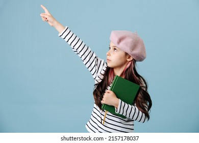 Pointing With Her Finger Tween Girl In French Beret Posing Over Blue Background. She Has Dyed Hair Strands. Side View.