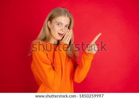 Pointing. Portrait of young caucasian woman isolated on red studio background with copyspace. Beautiful female model. Concept of human emotions, facial expression, sales, advertising, youth.