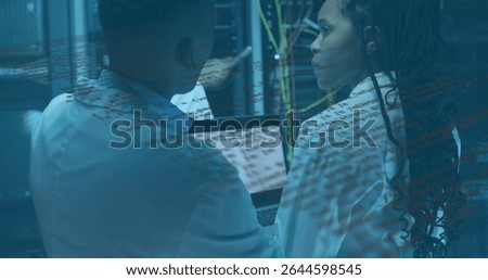 Pointing techs in lab coats examining server racks and Ethernet cables in server room, with laptop. Technology, data, infrastructure, cybersecurity, innovation, digital, networking